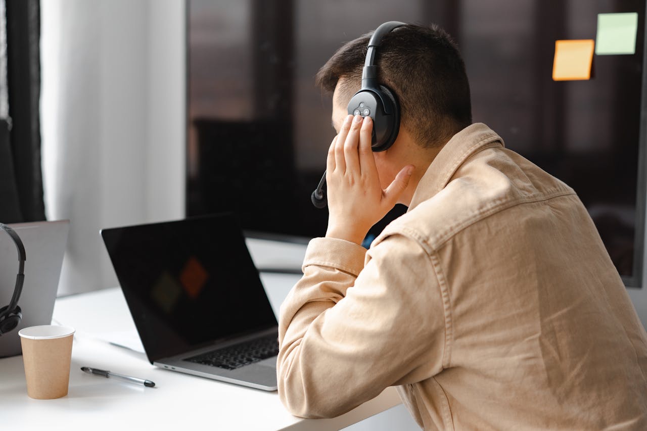 Home A man wearing headphones works at a laptop in a modern office setting.